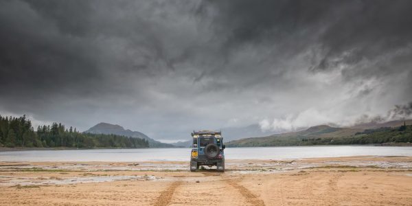 Land Rover on the shore of Loch Laggan beneath a dramatic stormy sky in the Scottish Highlands