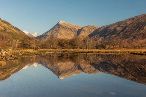 Panoramic photograph of Loch Etive in the Scottish Highlands, with mountains reflected in perfectly still water on a clear, sunny day.