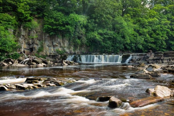 Richmond Falls on the River Swale in North Yorkshire, with cascading waterfalls, rocky riverbanks and green woodland.
